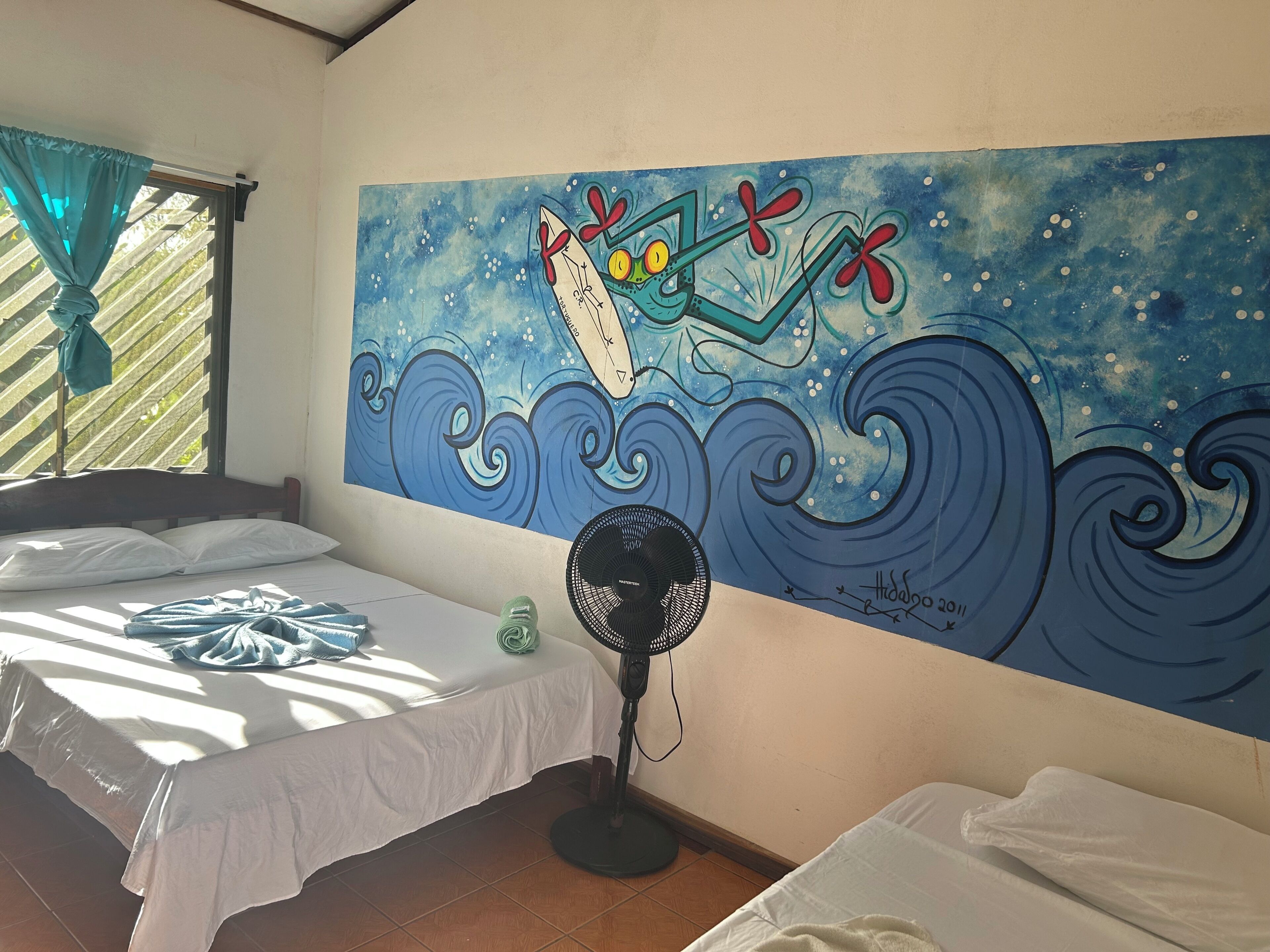 Quarto com duas camas, um ventilador e um mural grande na parede.