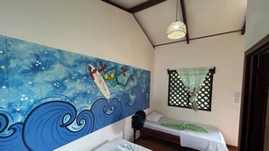 Une chambre avec deux lits, une fresque murale, un ventilateur et une fenêtre avec un treillis.