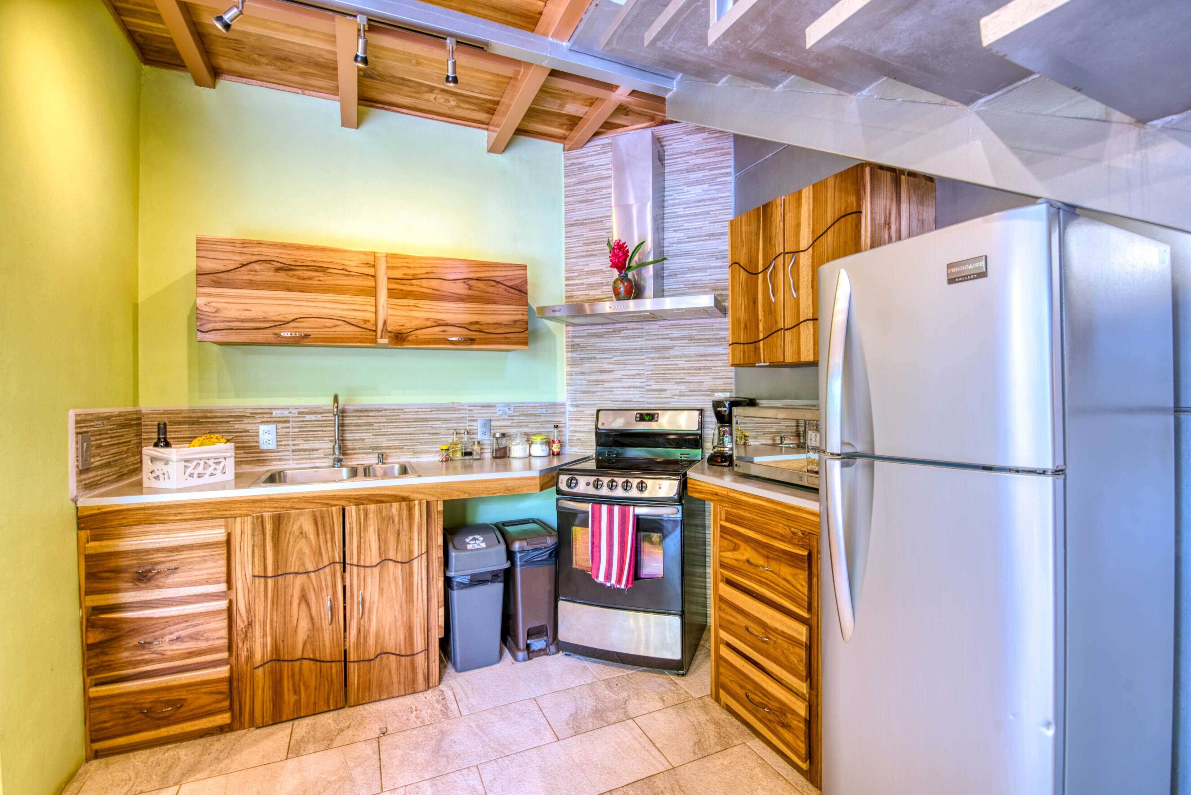 Una cocina con armarios de madera, un refrigerador de acero inoxidable, una estufa y un cubo de basura.