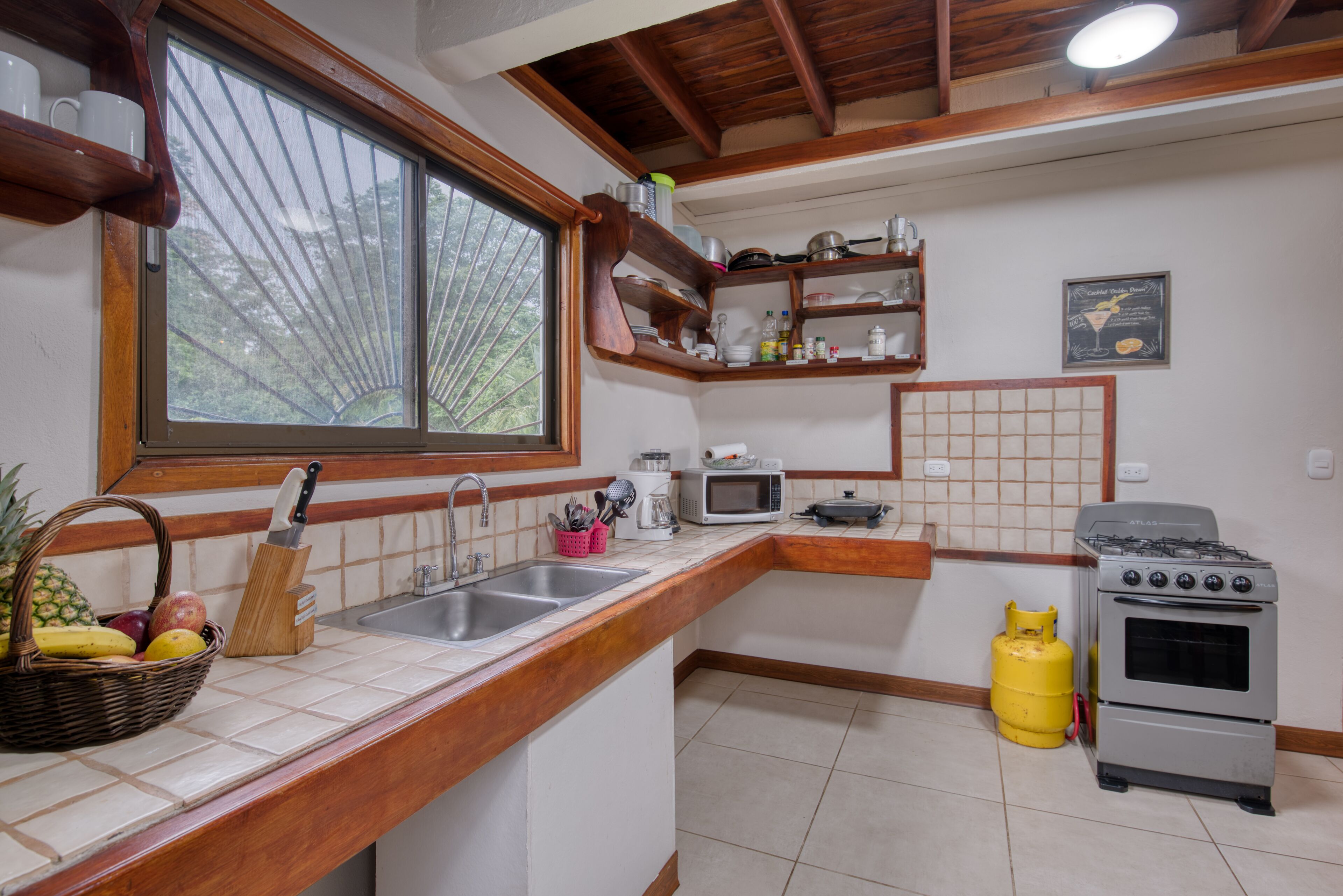 Una cocina con encimera de madera, un lavamanos, un microondas, una estufa a gas y una ventana con vistas a árboles.