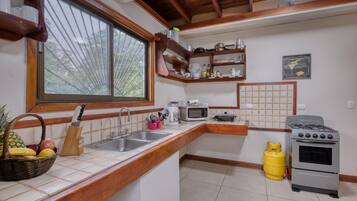 Una cocina con encimera de madera, un lavamanos, un microondas, una estufa a gas y una ventana con vistas a árboles.