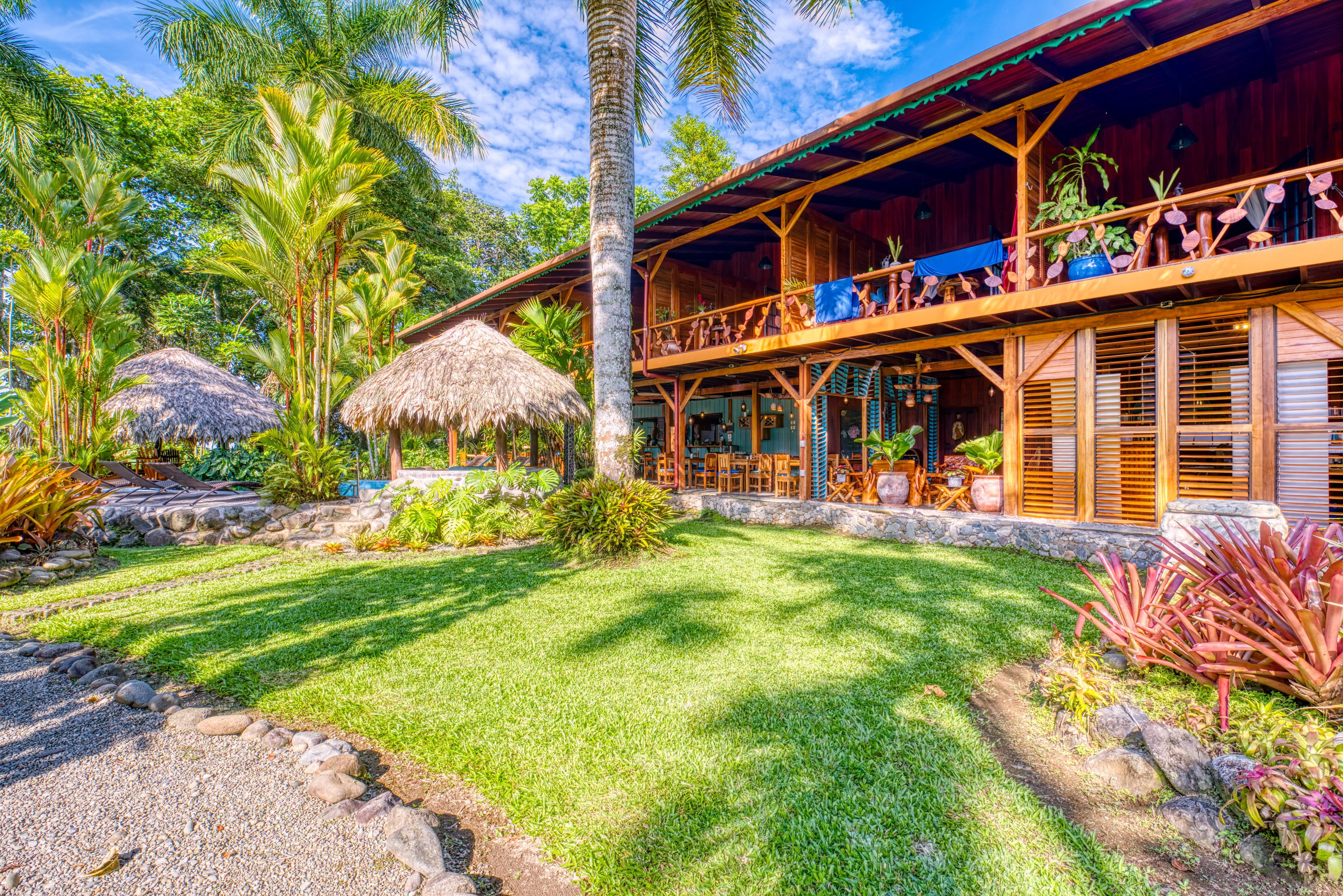 Un resort tropical con una veranda de techo de paja, abundante vegetación y un césped bien cuidado.