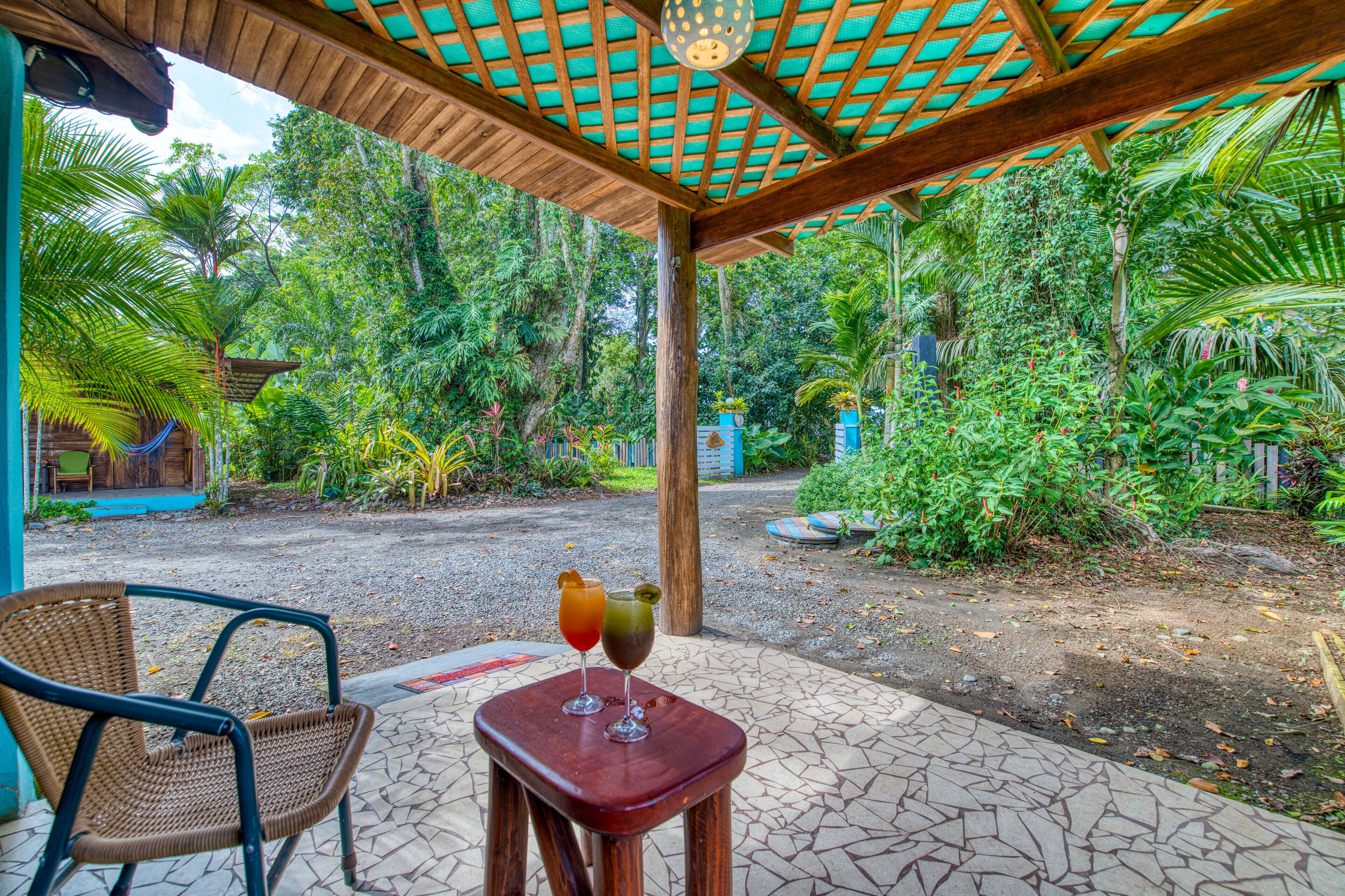 A covered outdoor area with a table and chairs, surrounded by lush greenery and a clear view of the surrounding forest.