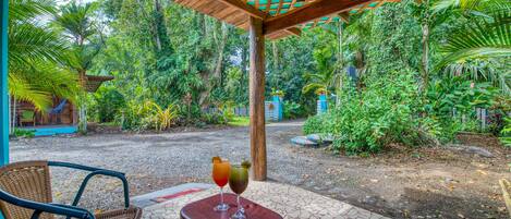 A covered outdoor area with a table and chairs, surrounded by lush greenery and a clear view of the surrounding forest.