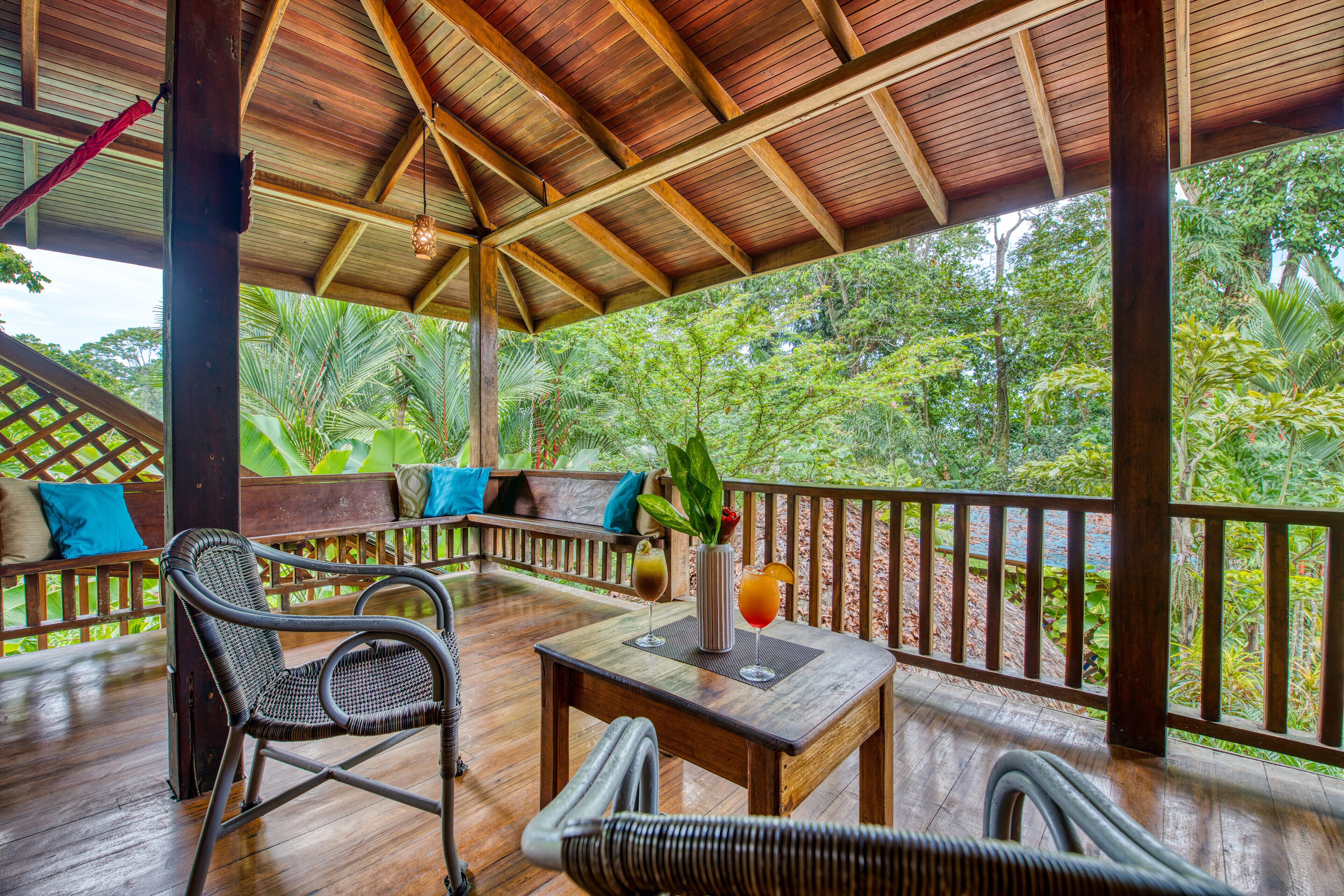 Une terrasse en bois avec des meubles en osier, une table avec des boissons et une vue sur une végétation luxuriante.