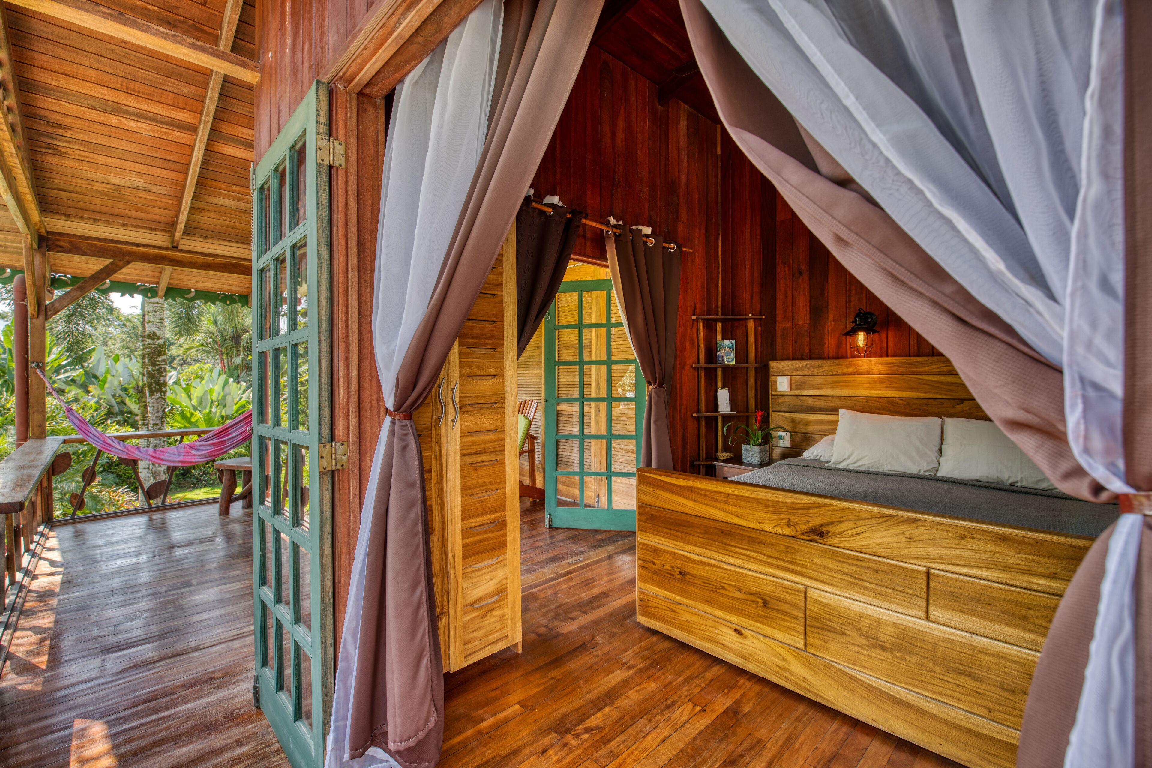 Una cabaña de madera con cama, cortinas y una hamaca.