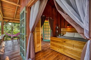 A wooden cabin with a bed, curtains, and a hammock. - Hotel Banana Azul - Adults Only (Cahuita)