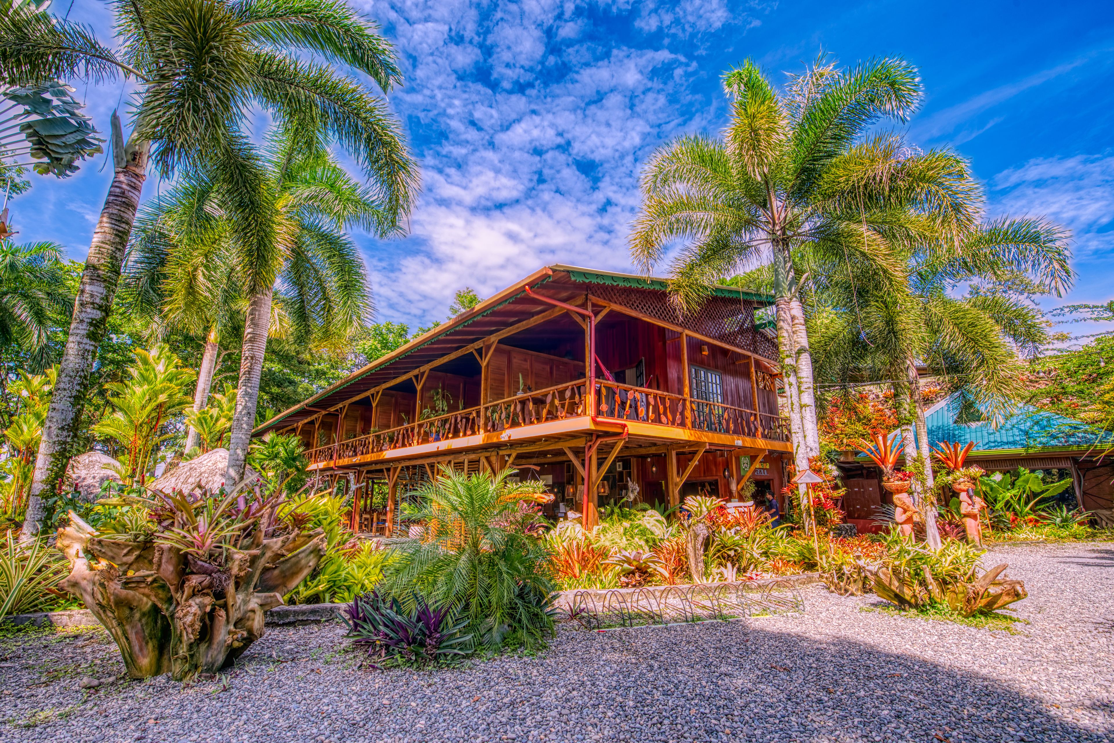 A wooden building with a balcony, surrounded by tropical plants and palm trees.