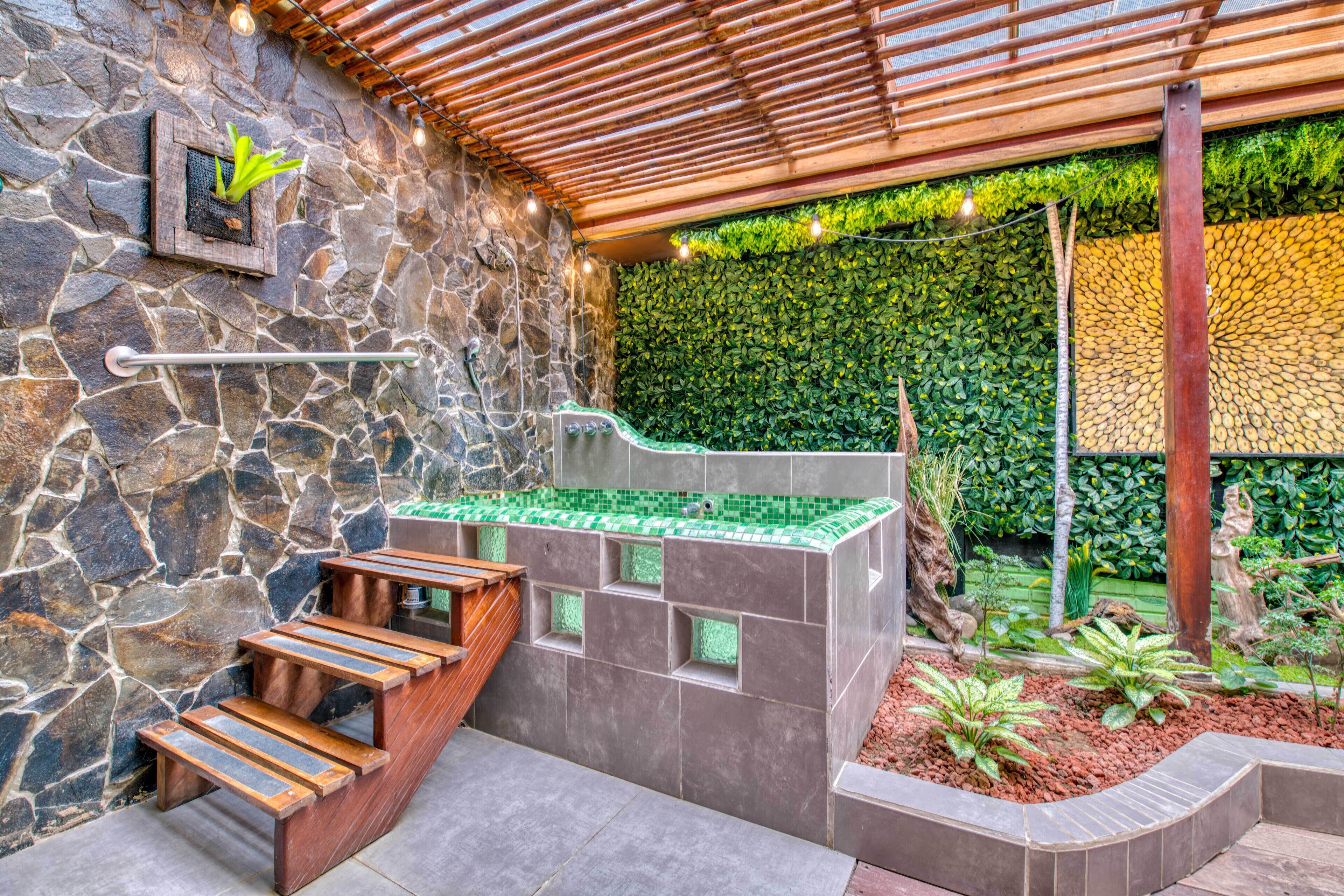 A stone wall with a wooden bench, a green-tiled water feature, and a wall of green foliage.