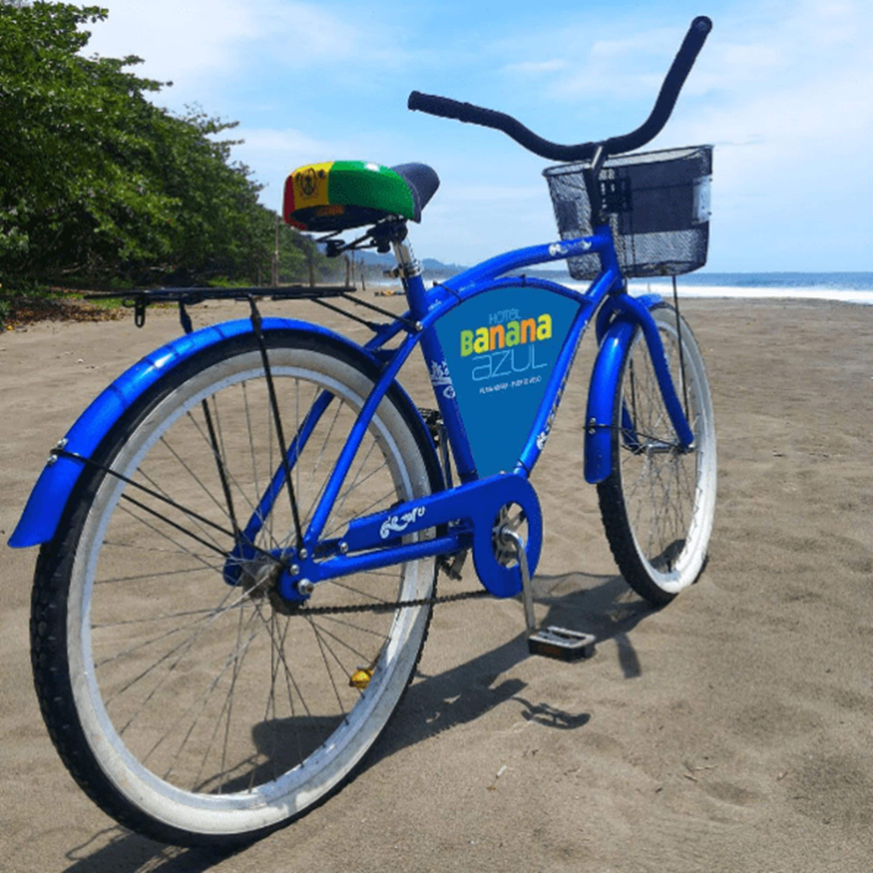 A blue bicycle with a basket and a green seat, parked on a sandy beach.