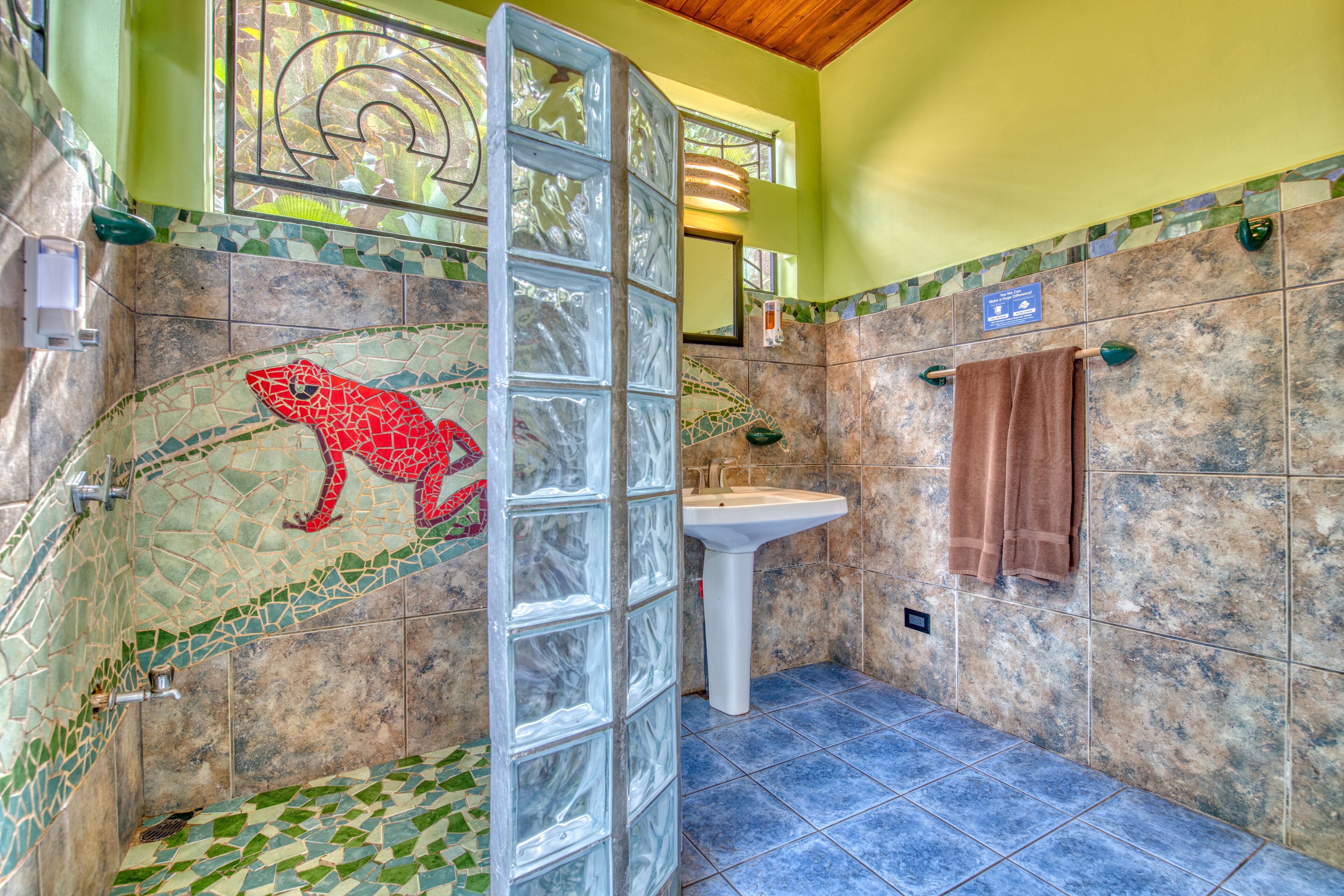 A bathroom with mosaic tile walls, a glass shower enclosure, a sink, and a towel rack.