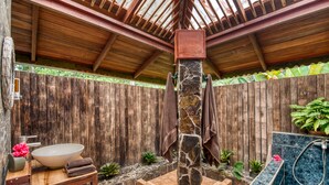 Techo de madera, un pilar de piedra, un banco de madera, pared de piedra y zona de ducha con azulejos.