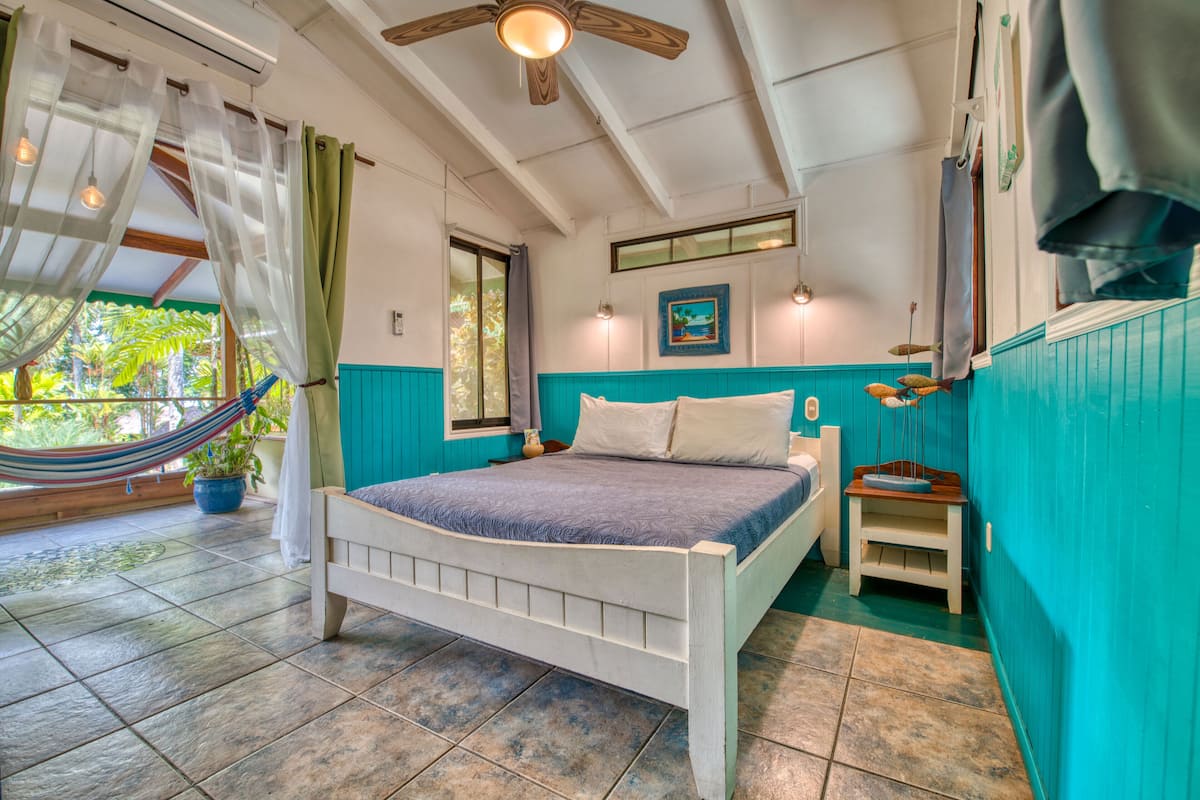 Une chambre avec un lit, une petite table de chevet, un hamac et une vue sur la verdure.