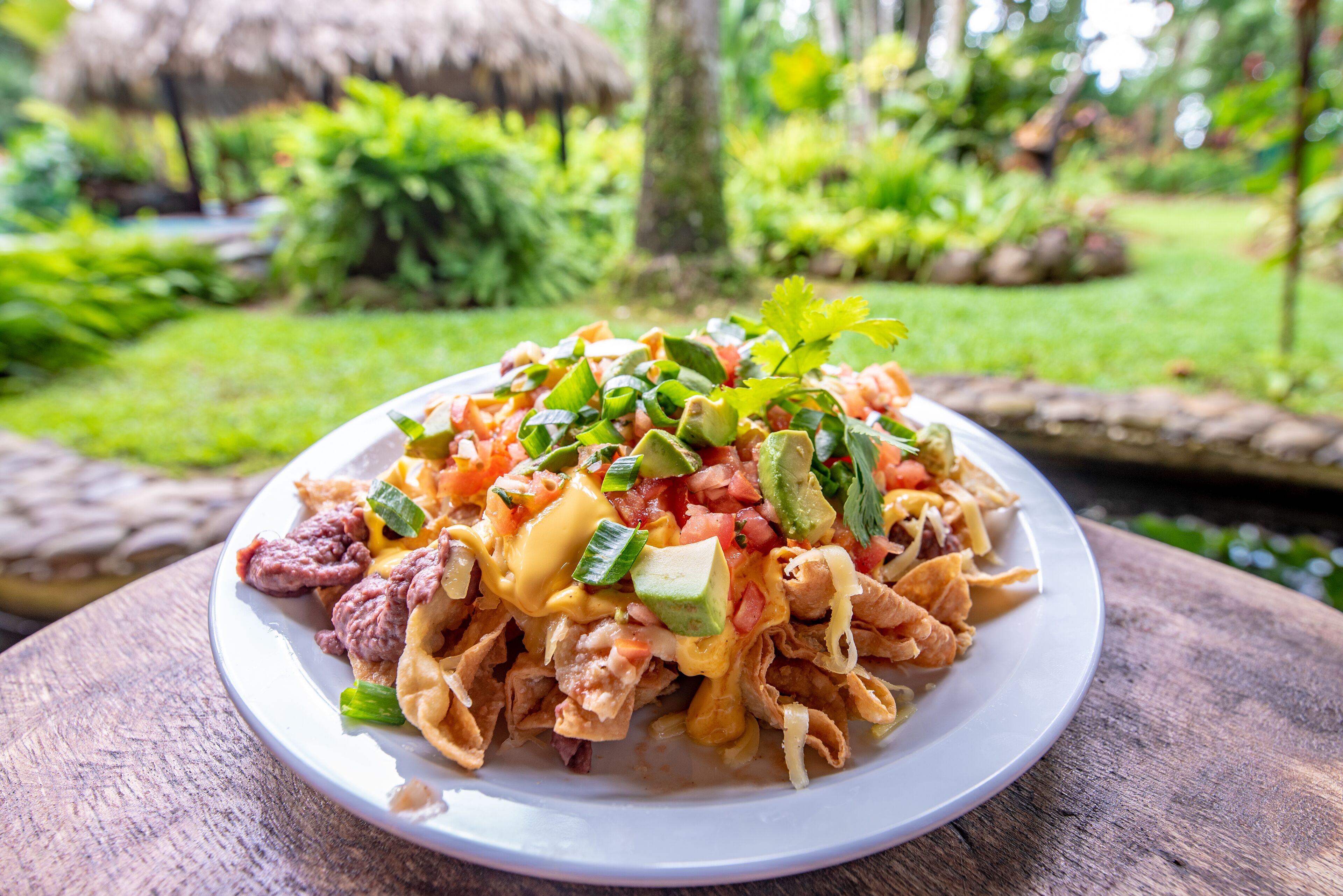 A plate of nachos with cheese, tomatoes, and green peppers on a wooden table.