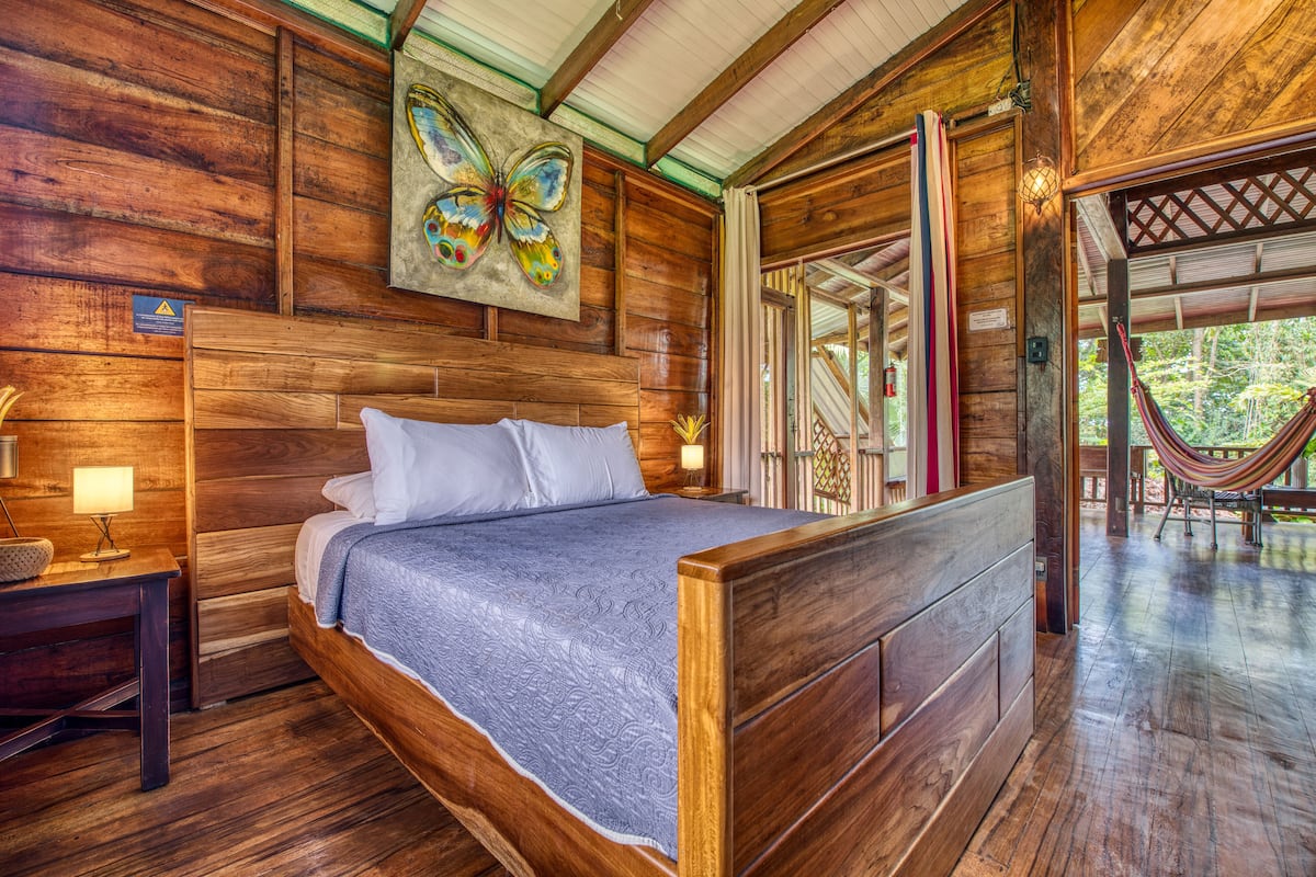 Une chambre à coucher en bois, avec un lit, des tables de chevet et un hamac.