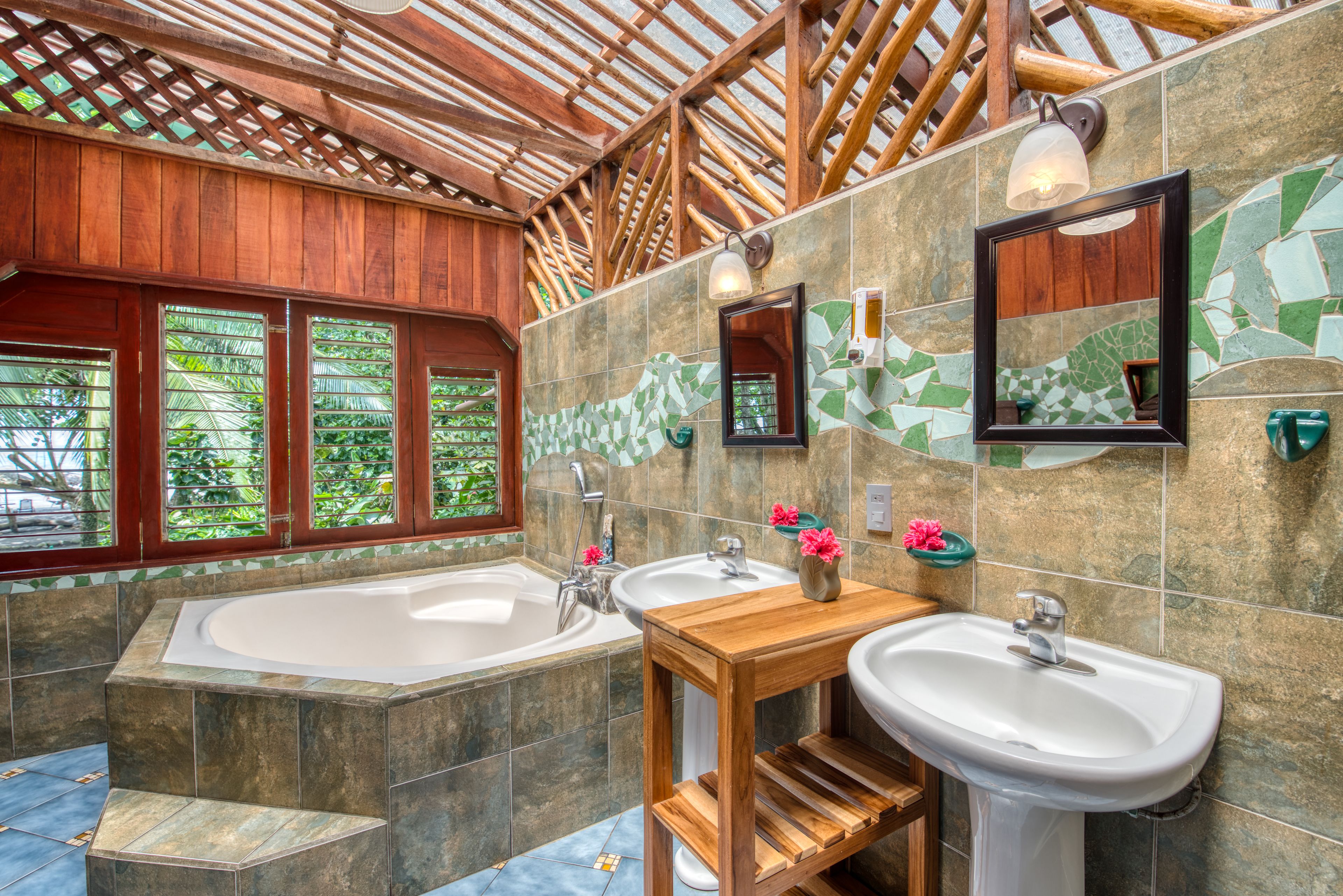 Un baño con techo de madera, dos lavamanos, una bañera grande y una pared de mosaicos.