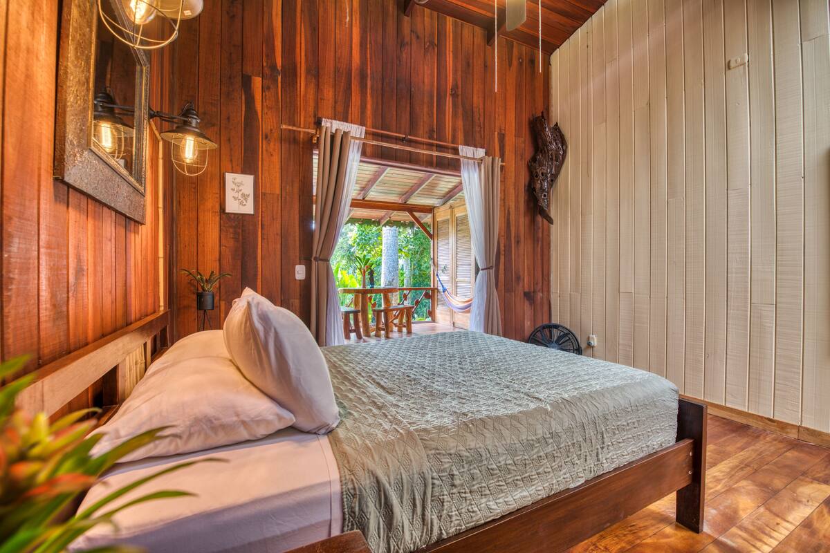 Une pièce en bois avec un lit, un luminaire suspendu et une vue sur l’extérieur.