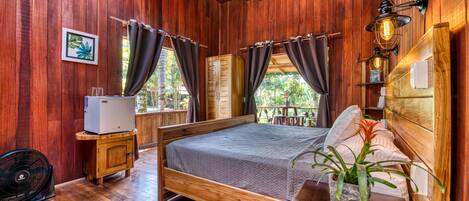 Una habitación de madera con una cama, un armario pequeño, un ventilador y un ventilador de techo.