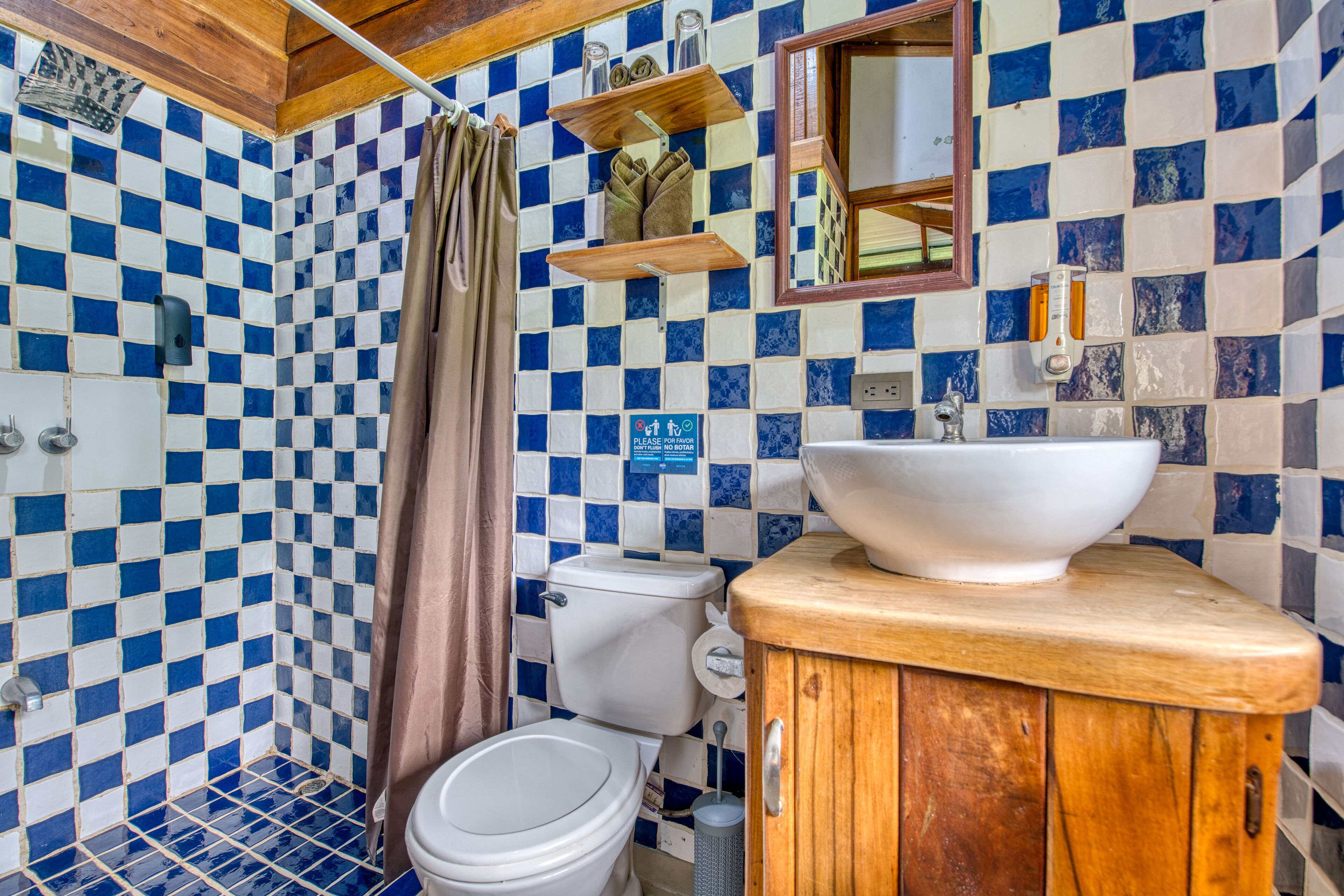 A bathroom with blue and white checkered tiles, a wooden cabinet, a white sink, and a toilet.