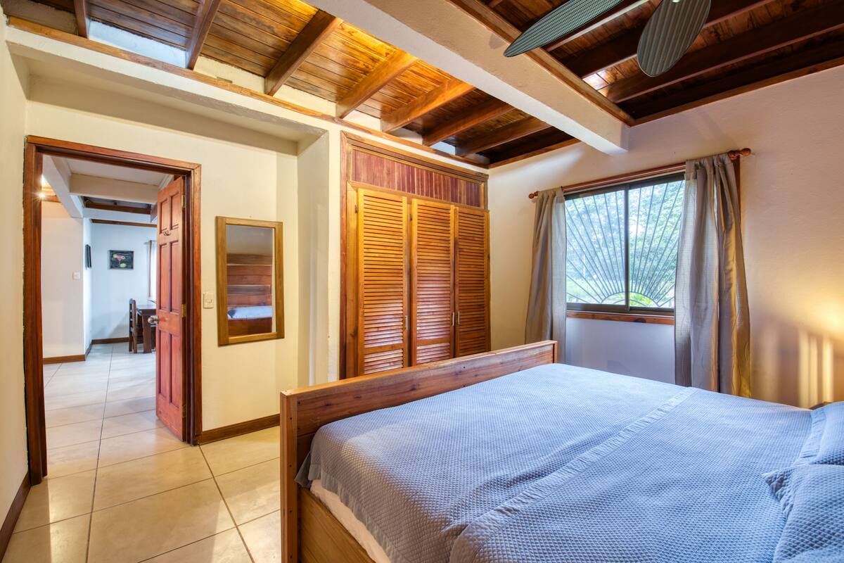 Une chambre à coucher avec un lit en bois, une armoire et une fenêtre avec des rideaux.