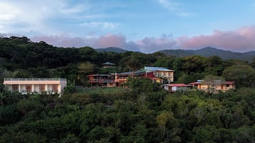 Il s’agit d’une propriété située sur une colline, comprenant plusieurs bâtiments, notamment une grande maison dotée d’un balcon et une construction plus petite avec un toit rouge.