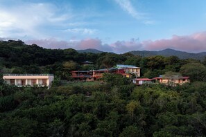 A hillside property with multiple buildings, including a large house with a balcony and a smaller structure with a red roof.