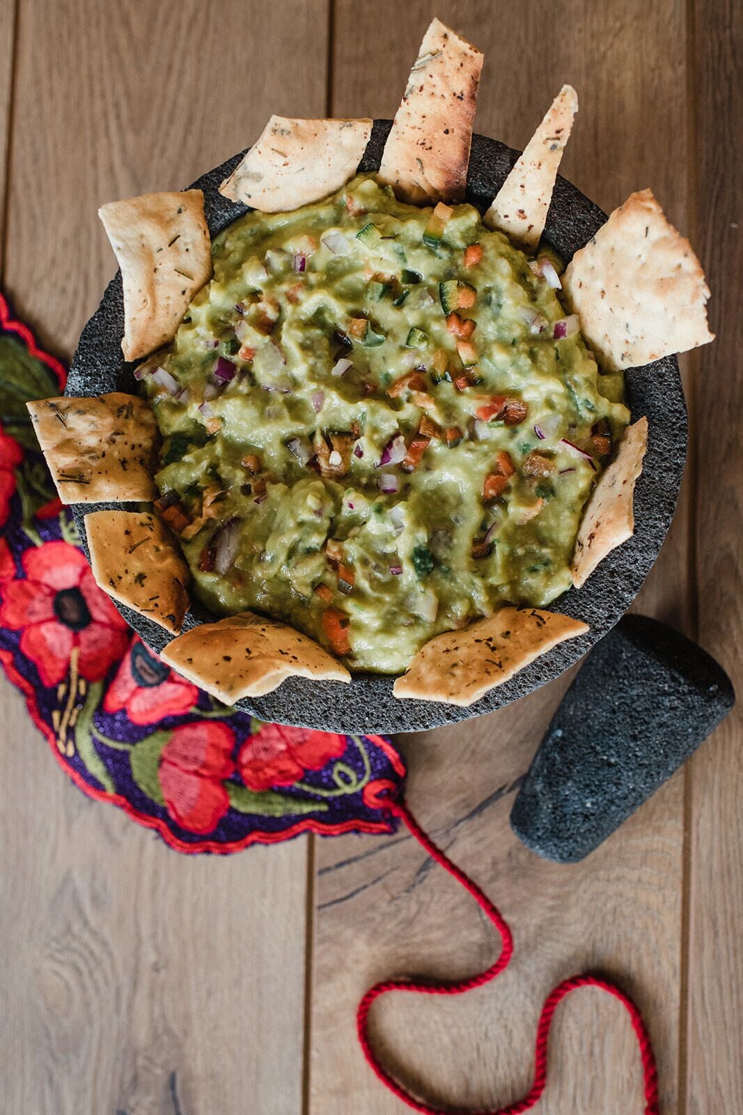 A bowl of guacamole with tortilla chips on a wooden table.