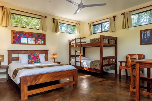 A room with a wooden bunk bed, a single bed, a wooden table, and a ceiling fan.