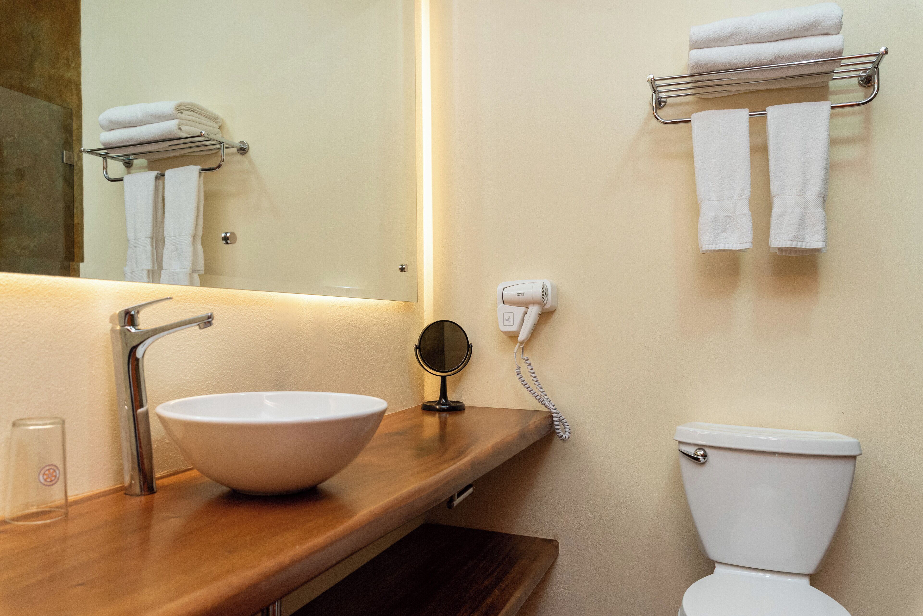 A bathroom with a wooden vanity, a white sink, a mirror, a towel rack, a toilet, and a wall-mounted phone.