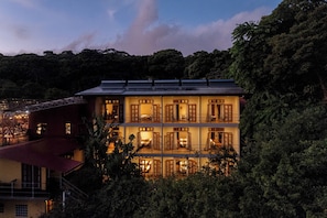 Een hotel met meerdere verdiepingen, uitgevoerd in traditionele architectuur, met diverse balkons en uitzicht op een weelderig bosgebied.