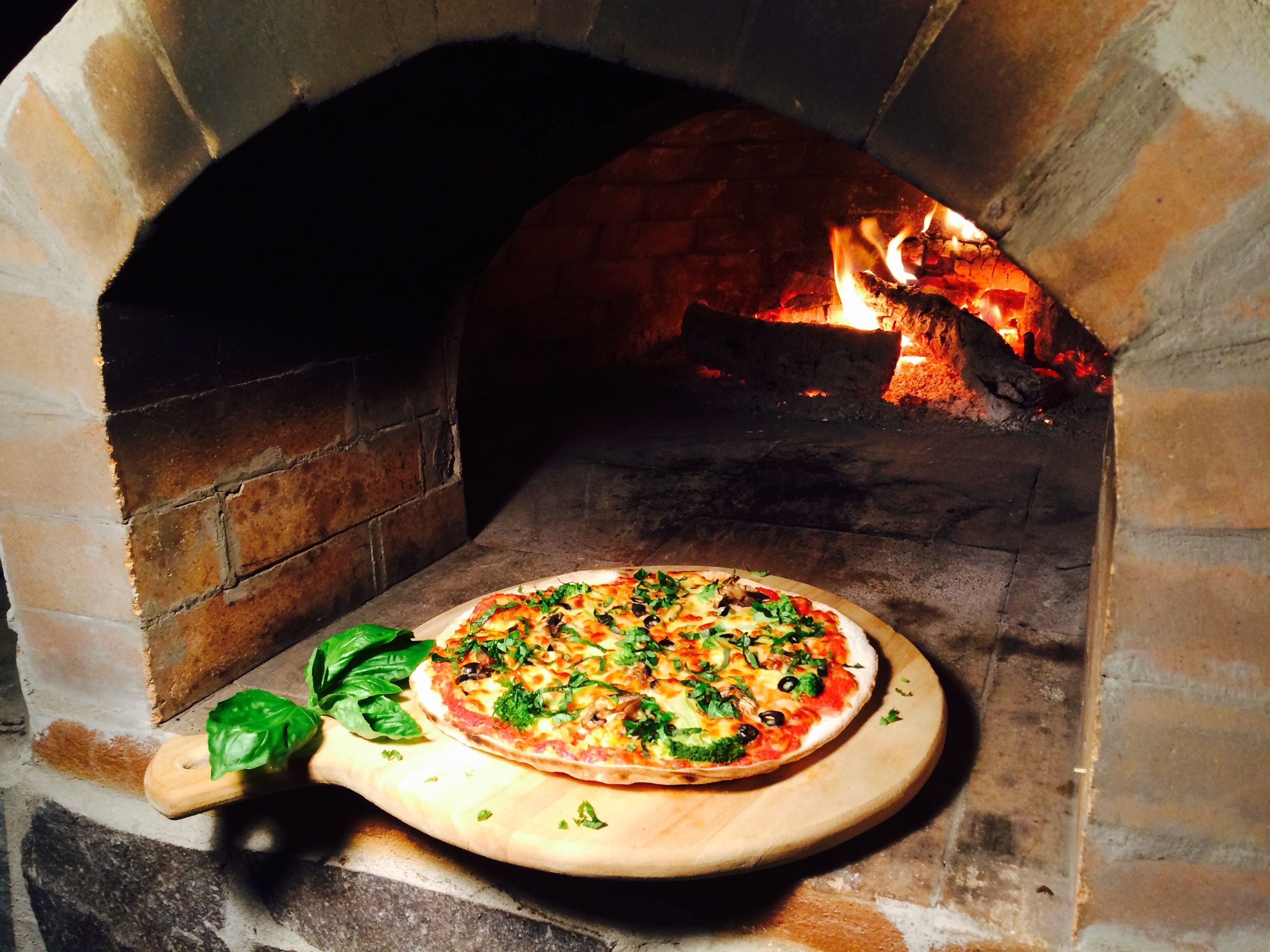 A pizza inside a brick oven with a fire burning in the background.