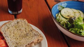 Un tavolo di legno con tre piatti di cibo, un bicchiere di bevanda rossa e una ciotola di insalata.