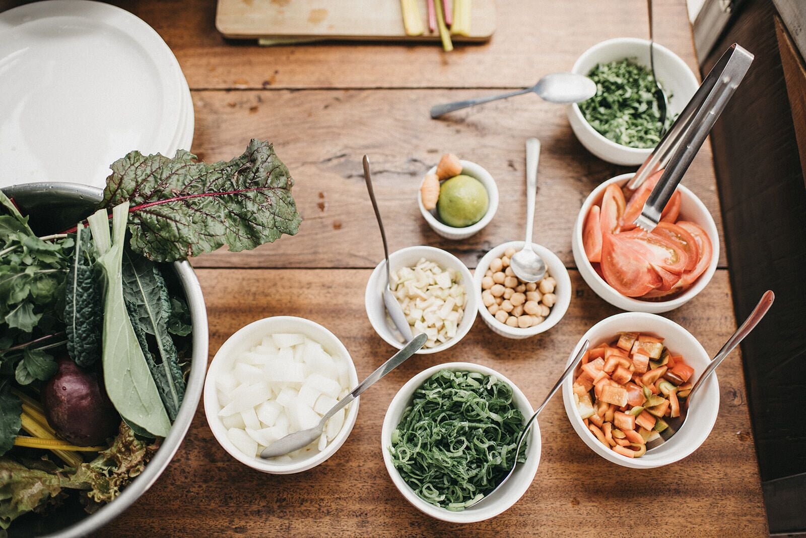 Una mesa de madera con varios recipientes que contienen diferentes alimentos, como verduras, garbanzos y una ensalada verde.