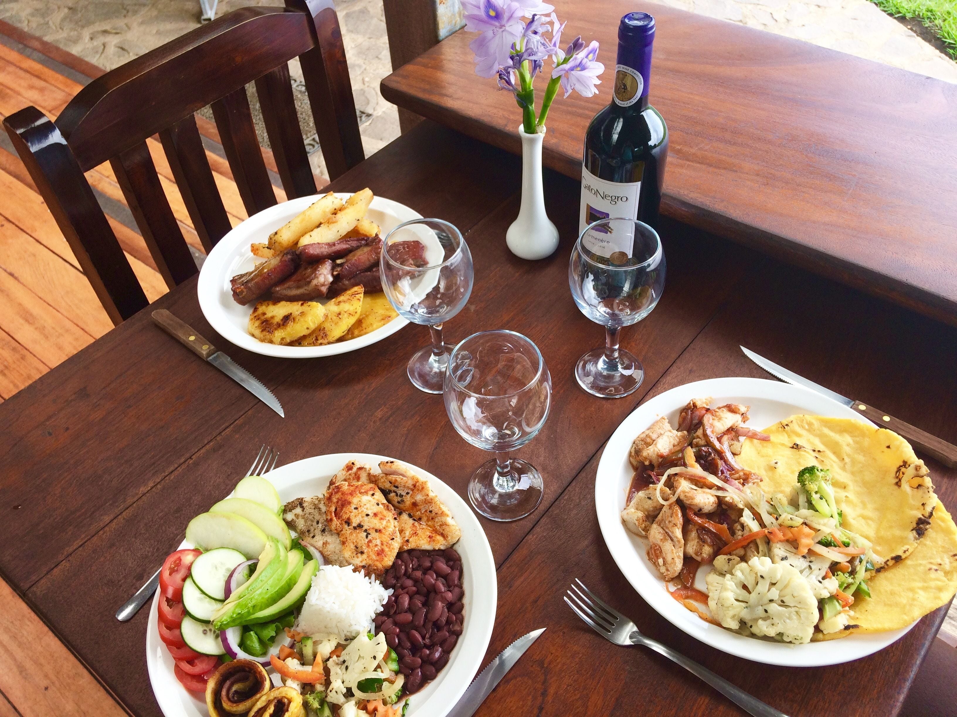A wooden dining table with plates of food, wine glasses, and cutlery.