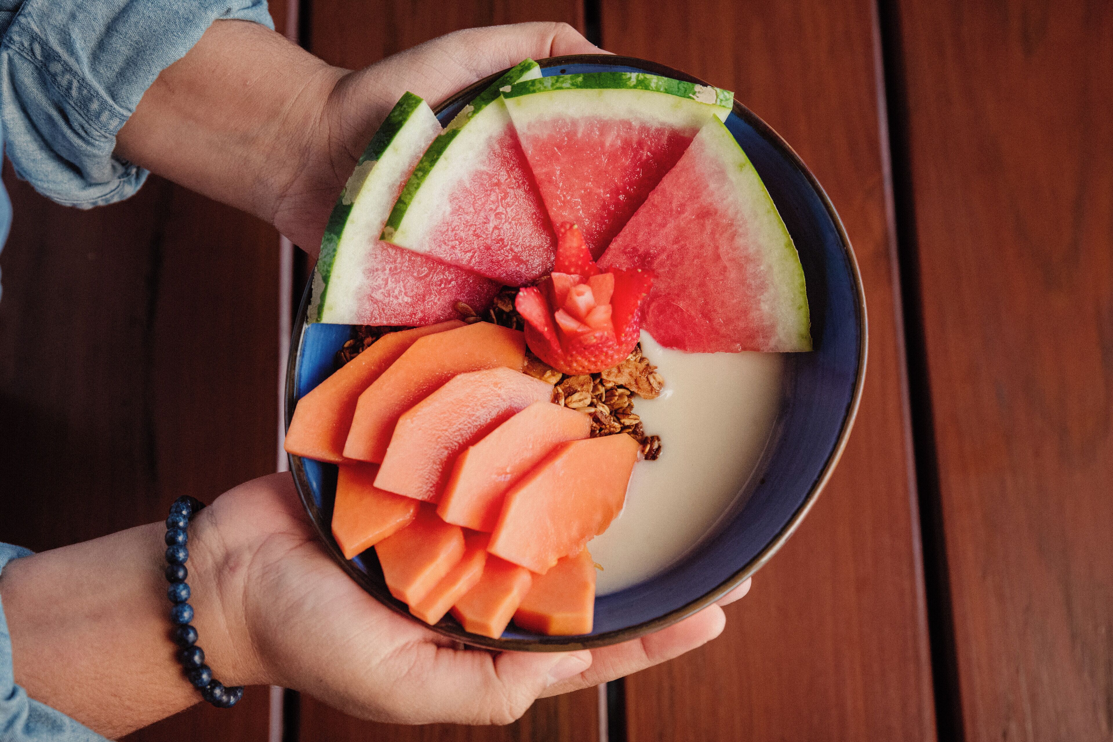 A person holding a bowl with watermelon slices, a carrot, and granola.