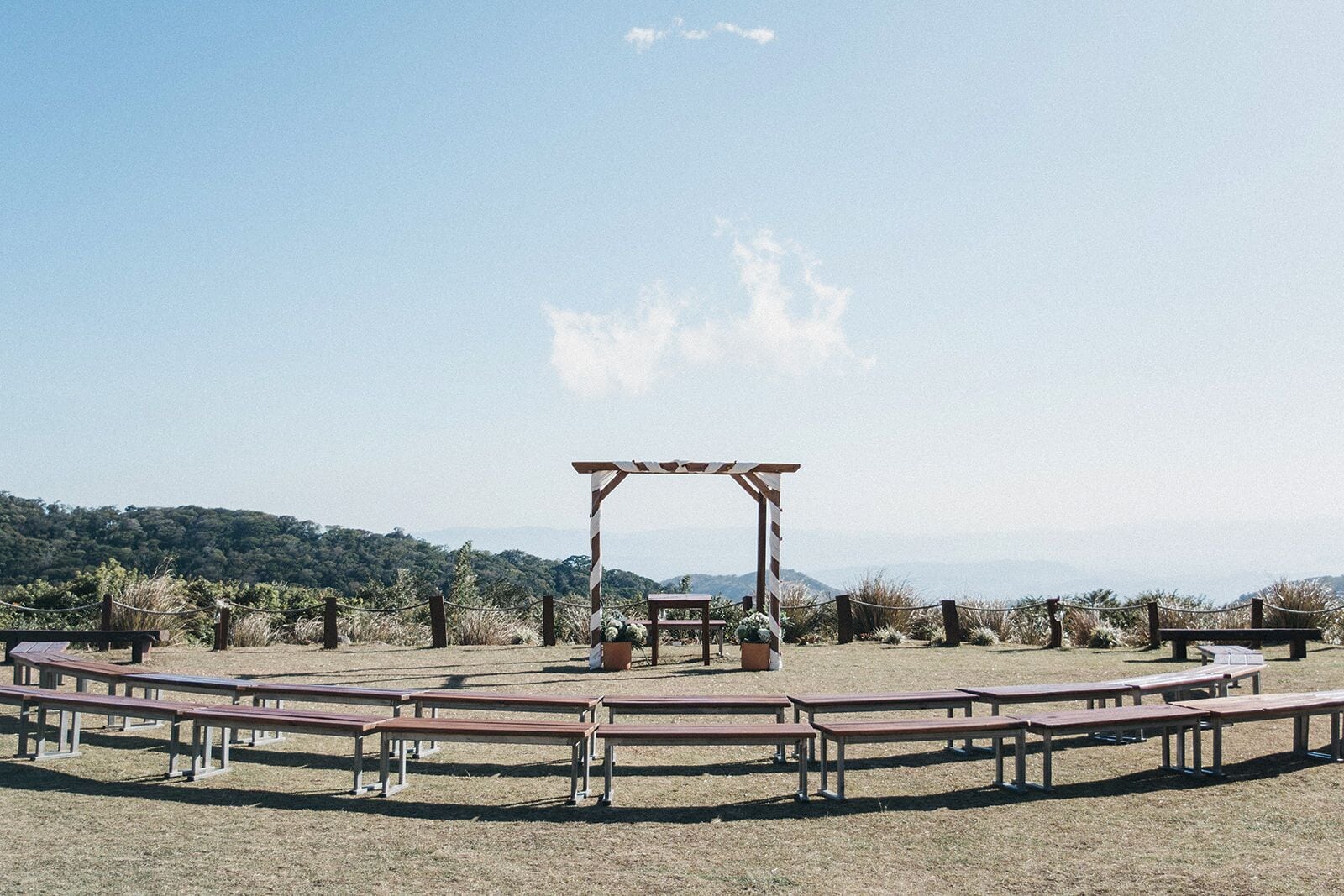 Un espace extérieur aménagé avec des tables de pique-nique et une pergola, le tout délimité par une barrière en corde.