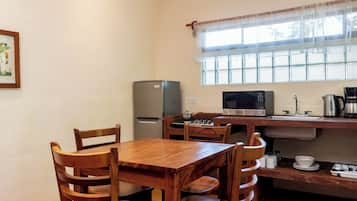A compact kitchen with a dining table, chairs, a refrigerator, a microwave, and a window with blinds.