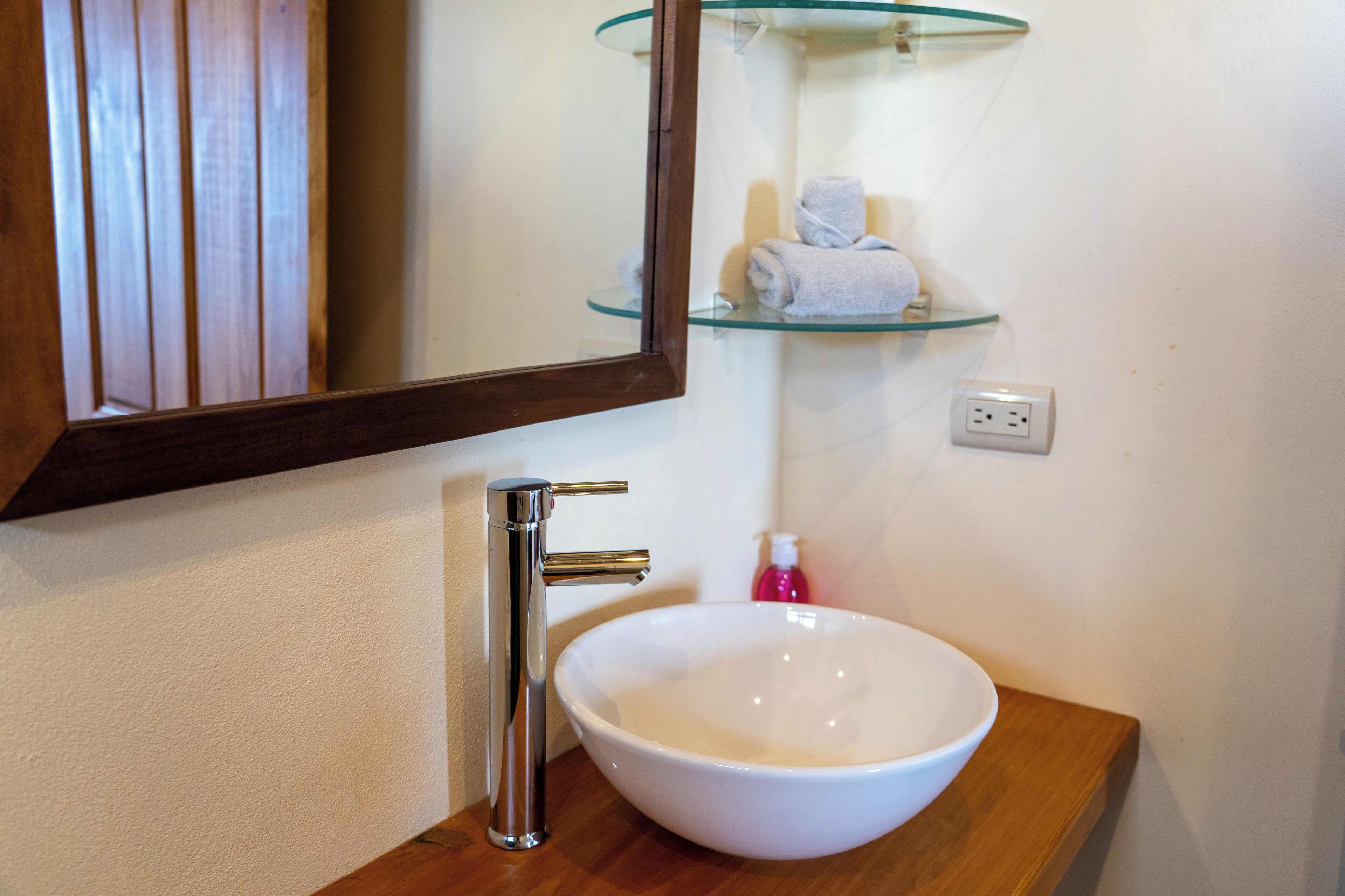 A bathroom with a white sink, chrome faucet, and a glass shelf above it.