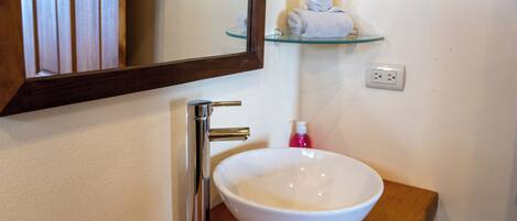 A bathroom with a white sink, chrome faucet, and a glass shelf above it.