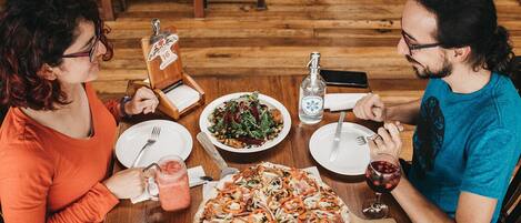 A wooden dining table with a pizza, salad, and drinks.