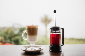 A coffee maker and a glass mug on a table with a blurred outdoor background.