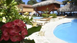 A poolside area with a thatched-roof structure, lounge chairs, and a clear blue pool. - Hotel SeaBreeze (Paraiso)