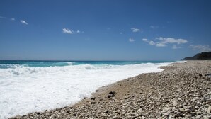 A rocky beach with waves crashing onto the shore under a clear blue sky. - Hotel SeaBreeze (Paraiso)