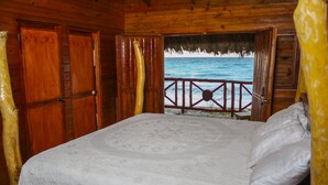 A wooden cabin room with a bed, a thatched-roof balcony, and a view of the ocean. - Hotel SeaBreeze (Paraiso)
