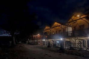A rustic log cabin with a wooden exterior and a thatched roof, illuminated by exterior lights. - Hotel SeaBreeze (Paraiso)