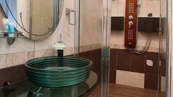 A bathroom with a glass sink, a shower enclosure, and a mirror.