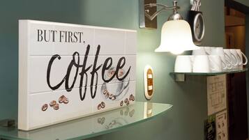 Un baño con un cuadro temático de café, un reloj y una repisa con tazas.
