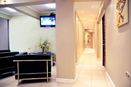 A hotel reception area with a reception desk, a television mounted on the wall, and a hallway leading to other rooms.