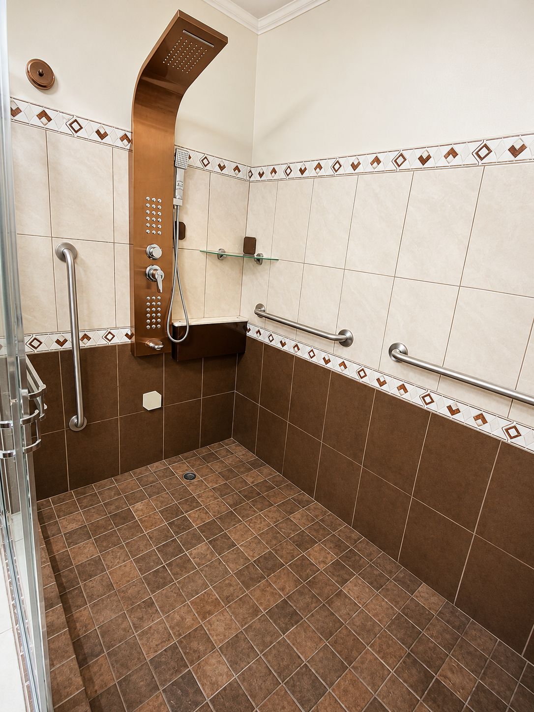 A shower area with a handheld showerhead, a glass shelf, and a grab bar.