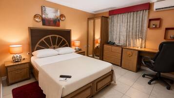 Una habitación de hotel con cama, mesitas de noche, un escritorio con silla, armario y ventana con cortinas.